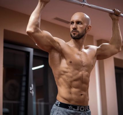 A bald, muscular man performing exercise on gym equipment indoors.